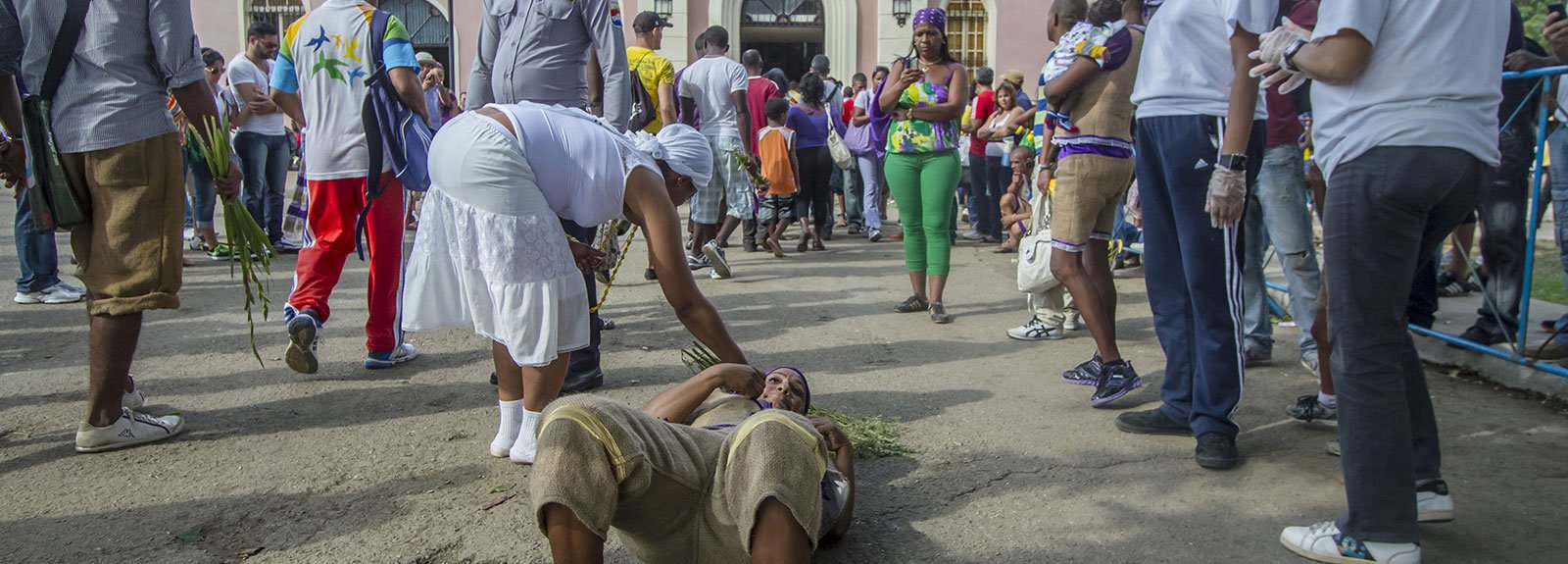 Woman lie down in front of a pink church surround by people
